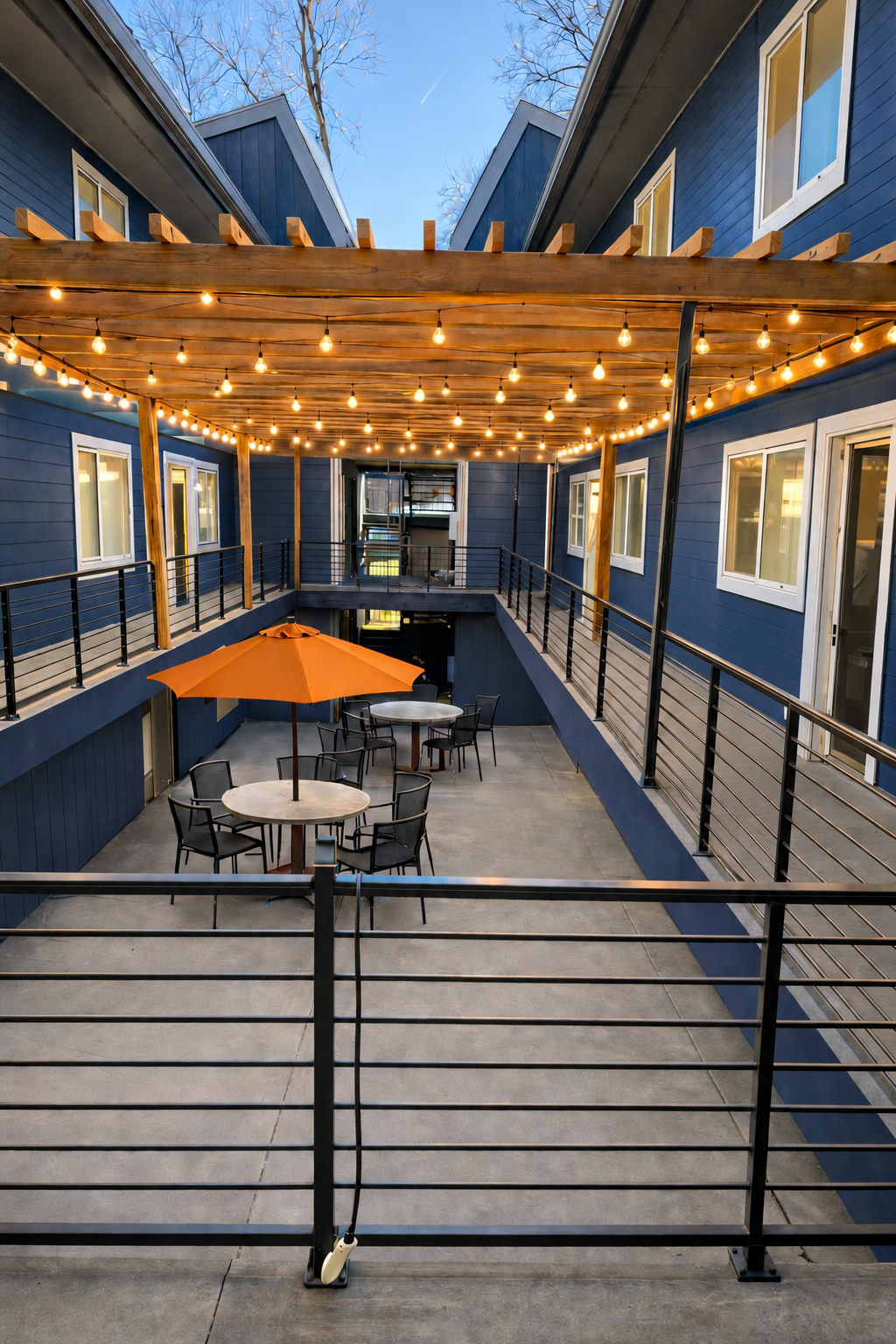 String-lit courtyard between two buildings of the cooperative, with cafe tables, an orange umbrella, and wooden pergola overhead